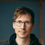 Jazz-Trompeter Johannes – Einzigartige Live-Musik für Ihre Events Porträt eines Jazz-Trompeters mit Brille, in lässigem Outfit, aufgenommen in einem Studio.