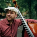 Max – Virtuoser Kontrabassist für Jazz-Events Porträt eines Kontrabassisten mit Schiebermütze, spielt im Freien, in einer entspannten Atmosphäre